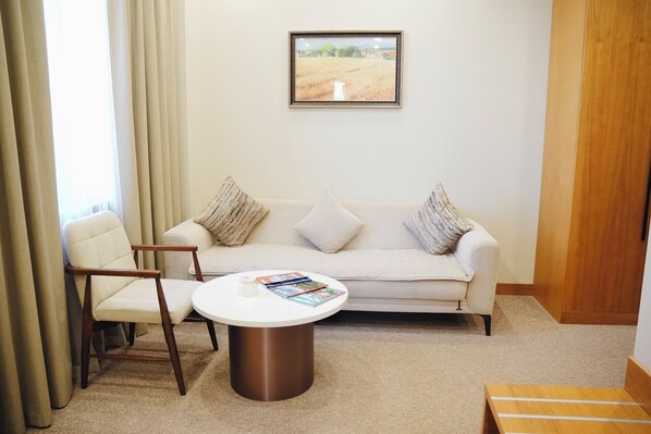 A room with a sofa, two armchairs, a coffee table, and a framed painting on the wall. - Mardan Hotel (Shymkent)