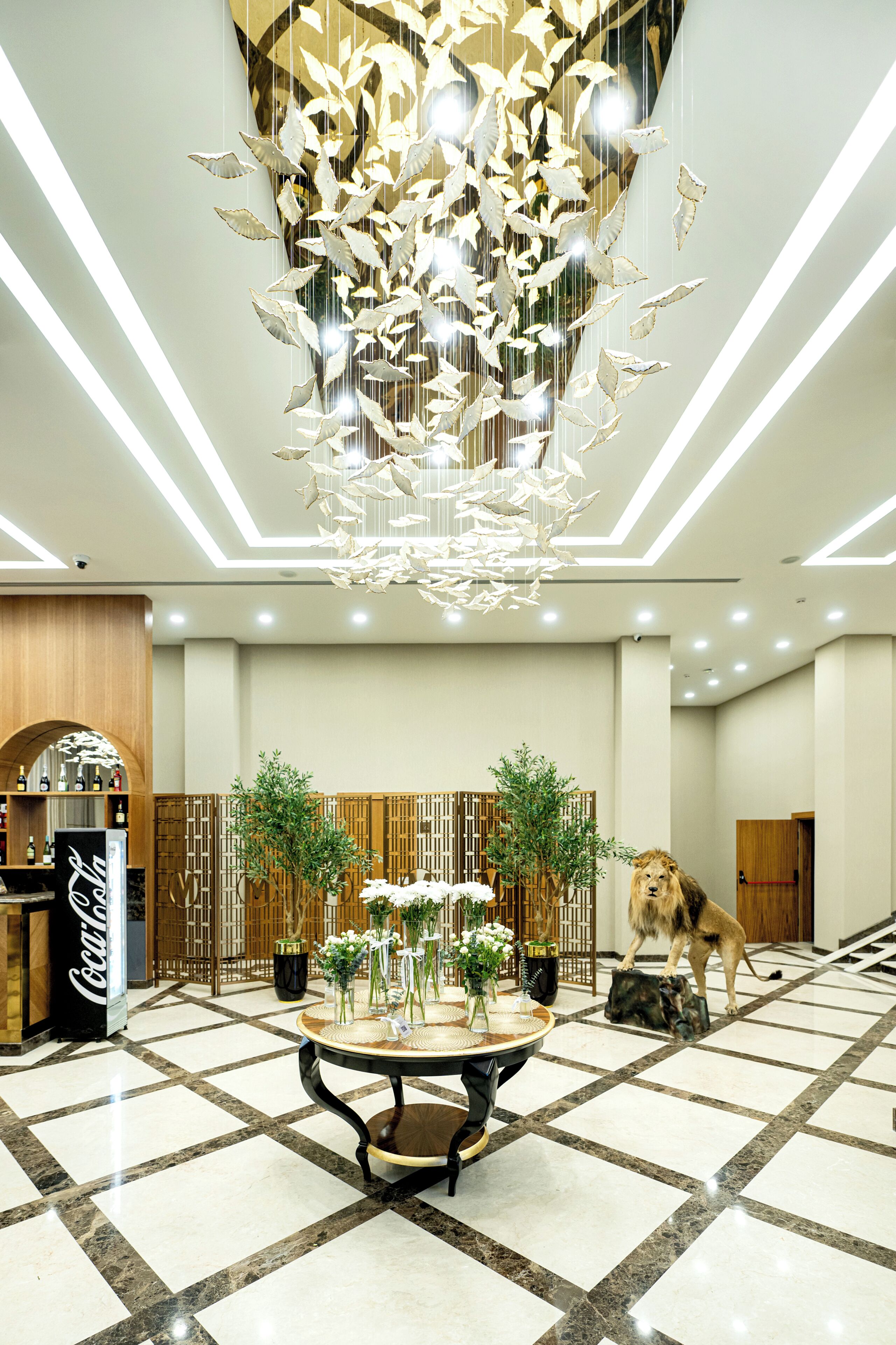 A lobby with a chandelier, a Coca-Cola refrigerator, a reception desk, and a lion statue.