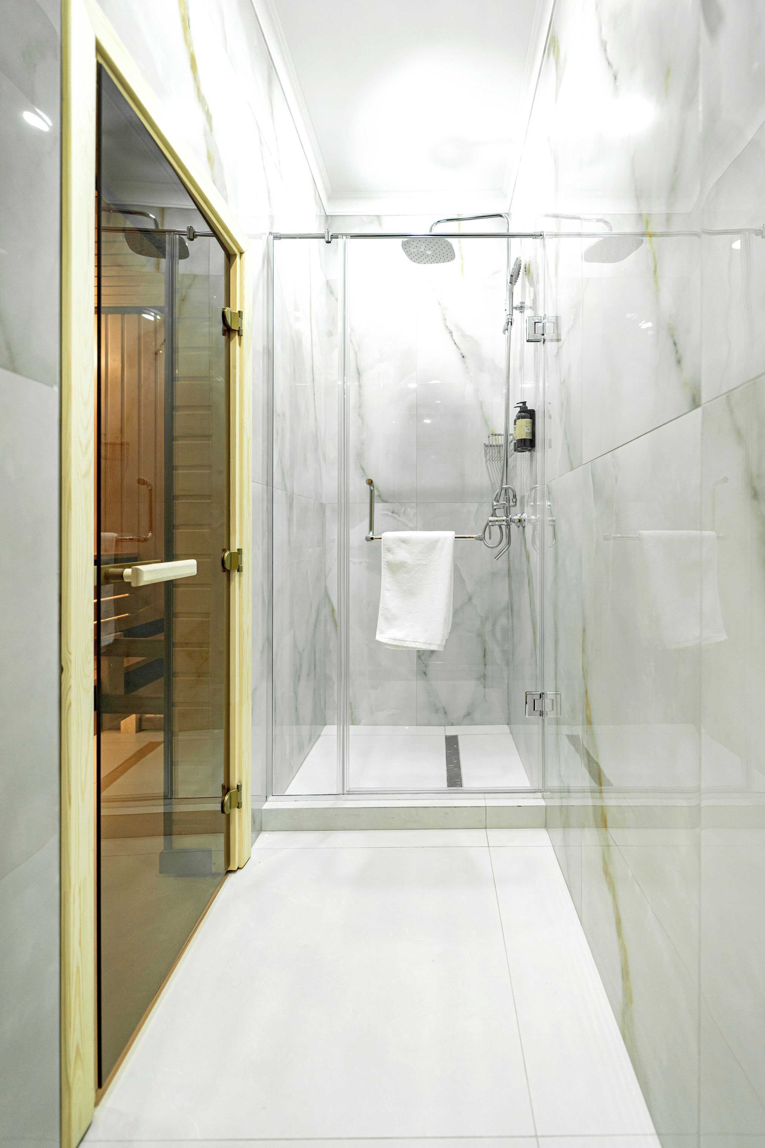 Een moderne badkamer met een douche in een glazen cabine, marmeren wanden en een houten deur.