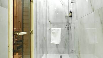 Een moderne badkamer met een douche in een glazen cabine, marmeren wanden en een houten deur.