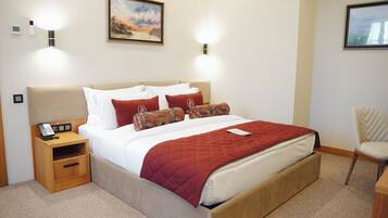 A neatly made bed with a red blanket, a bedside phone, and a small wooden nightstand.