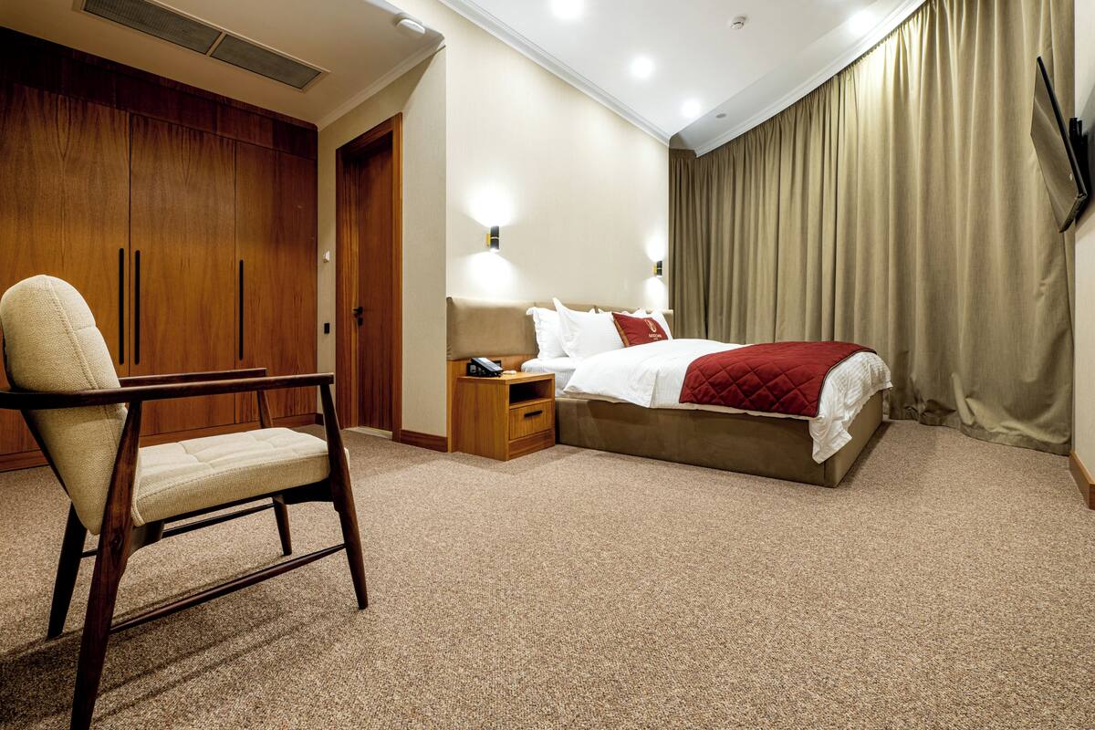 A hotel room with a bed, a chair, a nightstand, and a wardrobe.
