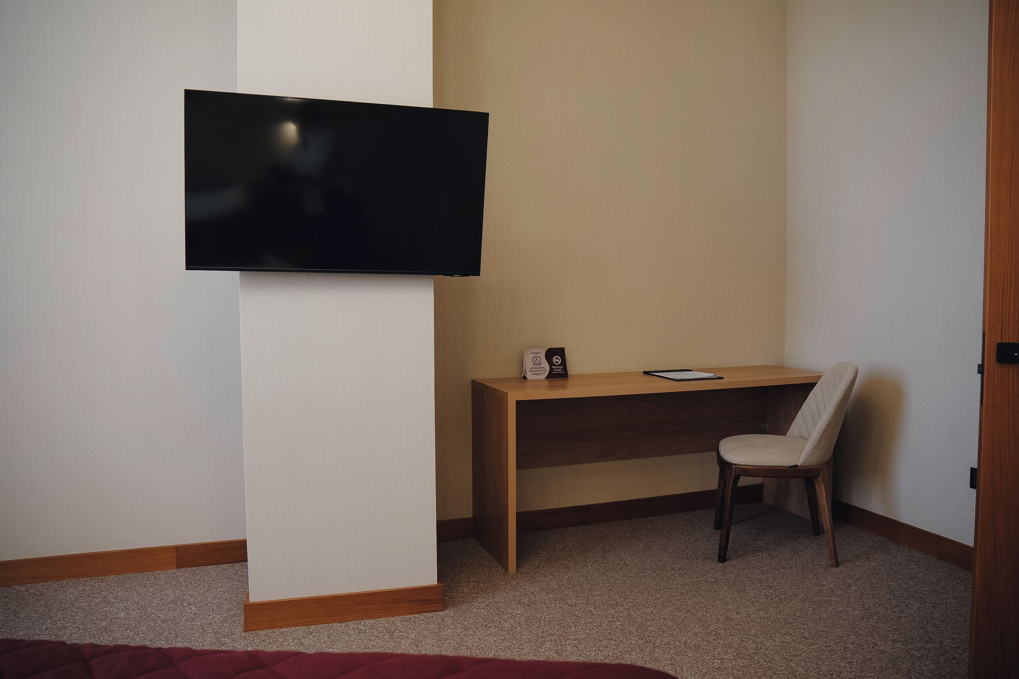 Une chambre d’hôtel équipée d’un téléviseur fixé au mur, d’un bureau en bois, d’une chaise et d’un lit recouvert d’une couverture rouge.