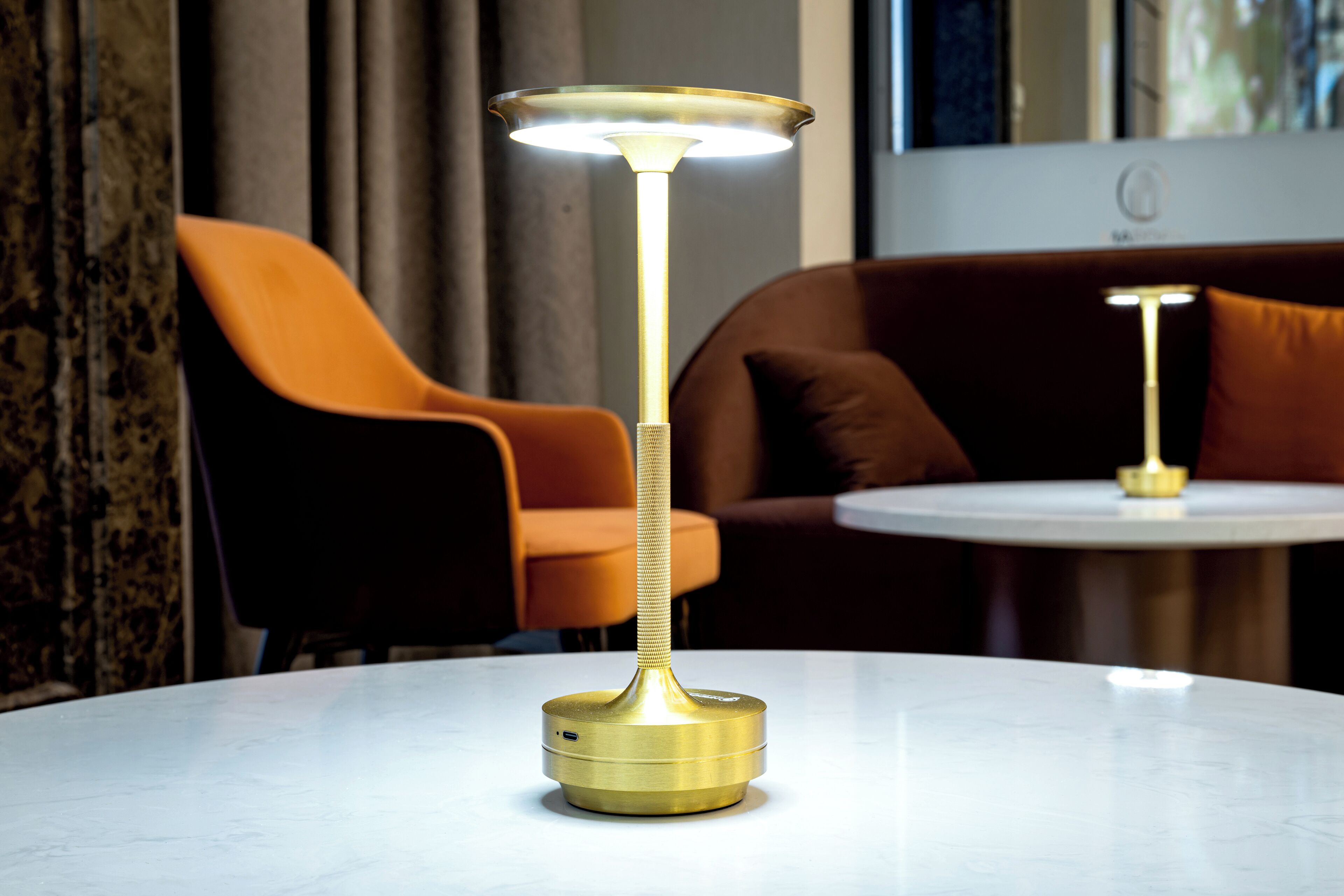 Una lámpara moderna sobre una mesa blanca en una habitación con una mesa redonda blanca y sillas naranjas.