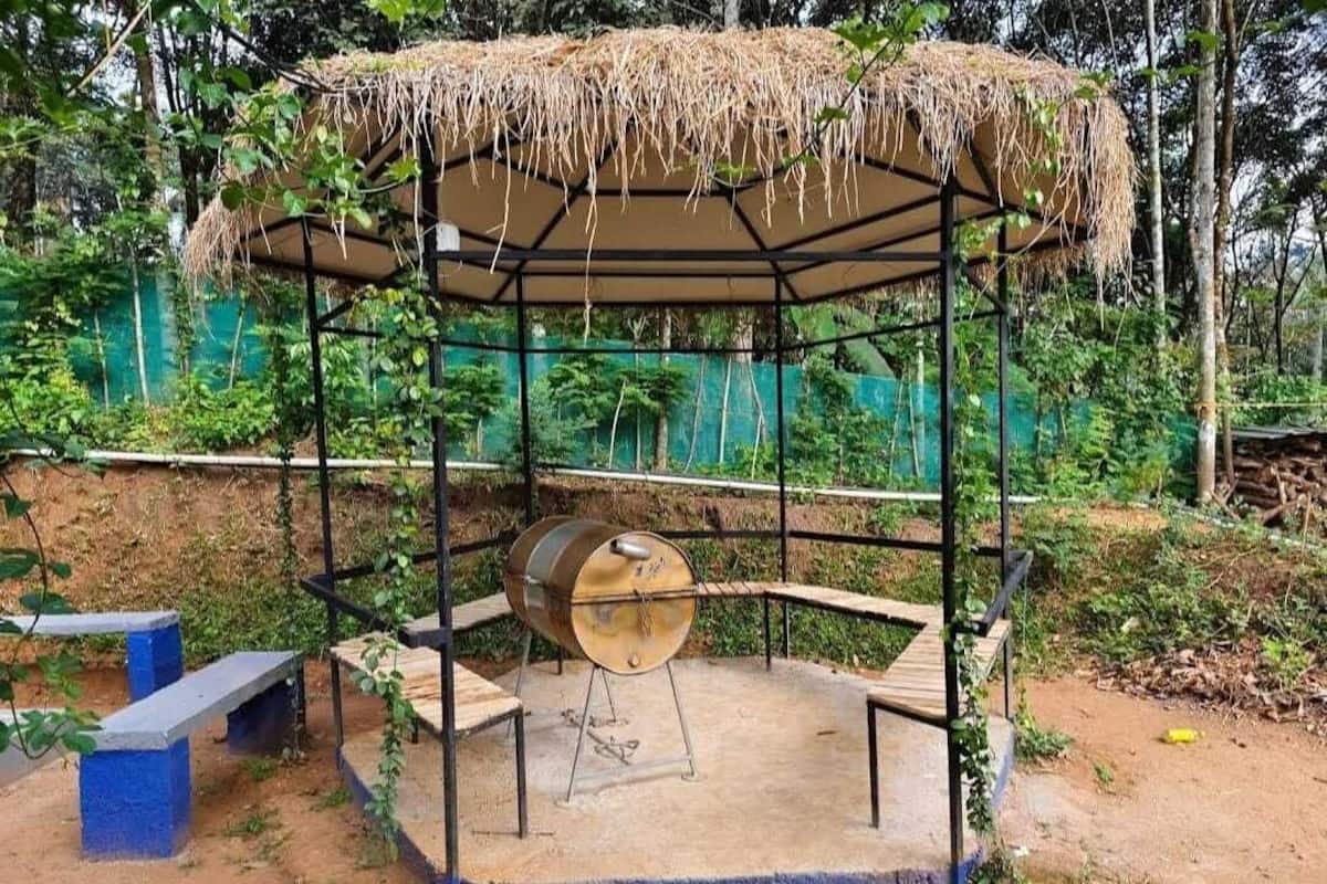 A barbecue setup with a metal barrel grill, a thatched roof, and a bench.