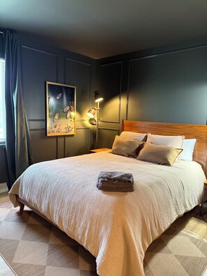 A neatly made bed with a folded towel, a bedside lamp, and a painting on the wall. - The Almond Joy • Modern Lakeside Retreat (Delavan)