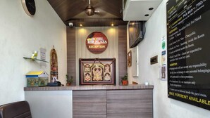A hotel reception area with a reception desk, a framed religious picture, a clock, and a wall with hotel rules and amenities listed. - HOTEL RSB PLAZA  (Tirupur)
