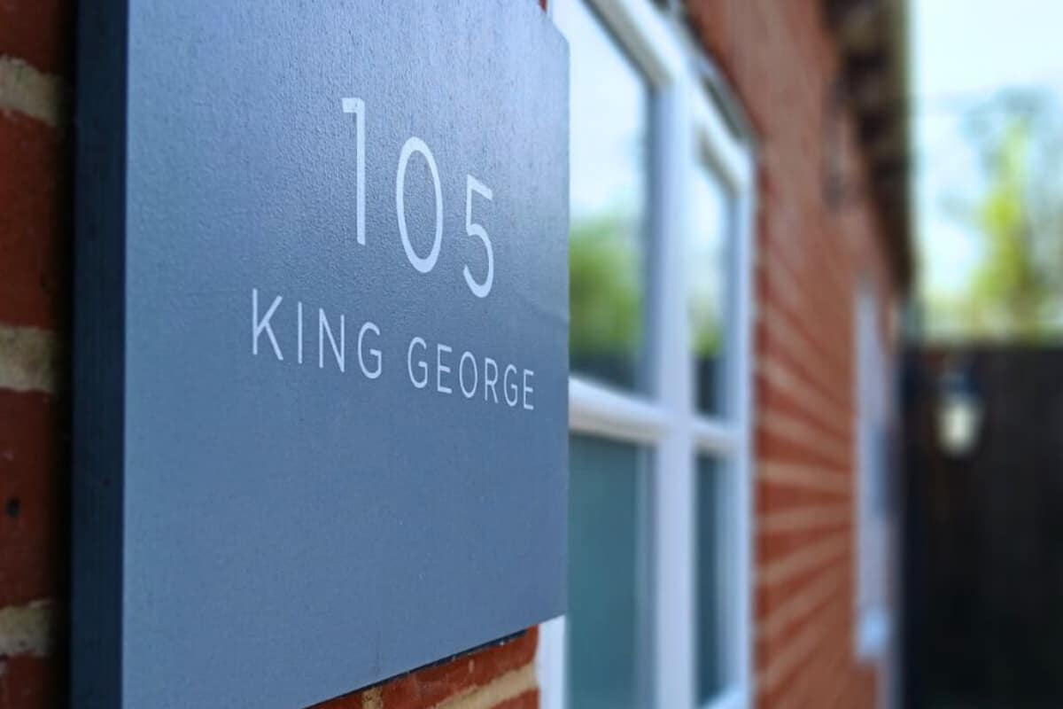 A house number sign with "105 KING GEORGE" on a brick wall.