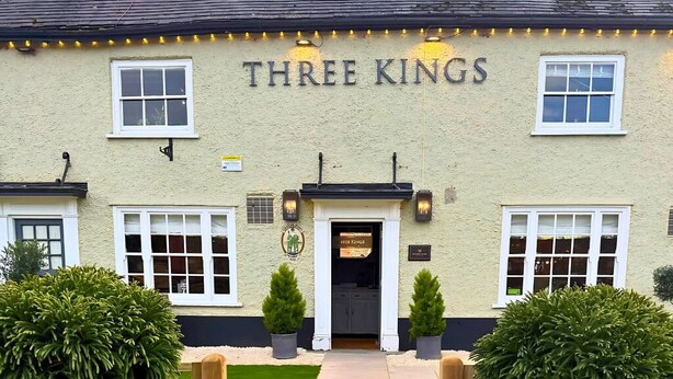 A building named "Three Kings" with a sign above the entrance, a small garden with potted plants, and a wooden gate. - Three Kings (Fornham All Saints)