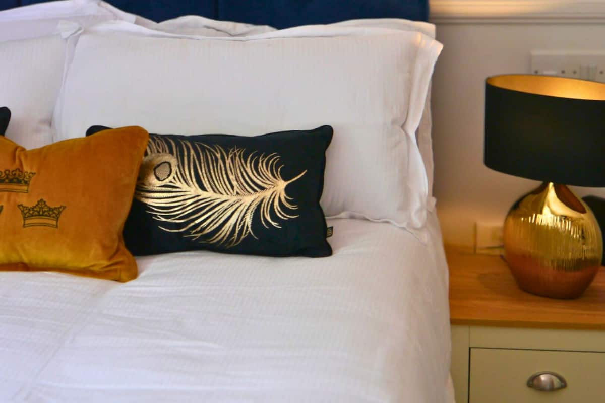 A neatly made bed with white linens and decorative pillows, a blue headboard, and a bedside table with a lamp.