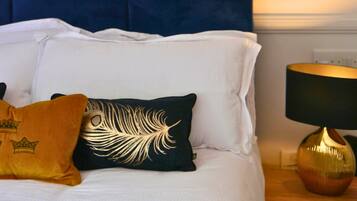 A neatly made bed with white linens and decorative pillows, a blue headboard, and a bedside table with a lamp.