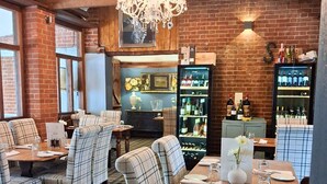A restaurant with plaid chairs, a wooden table set with plates and glasses, and a wine cooler in the background. - Three Kings (Fornham All Saints)