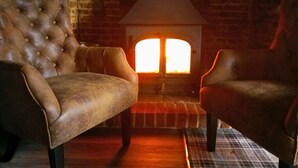 A cozy room with a brick fireplace, two leather armchairs, and a plaid rug. - Three Kings (Fornham All Saints)