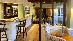 A cozy bar area with wooden stools, a counter, and a seating area with a fireplace. - Three Kings (Fornham All Saints)