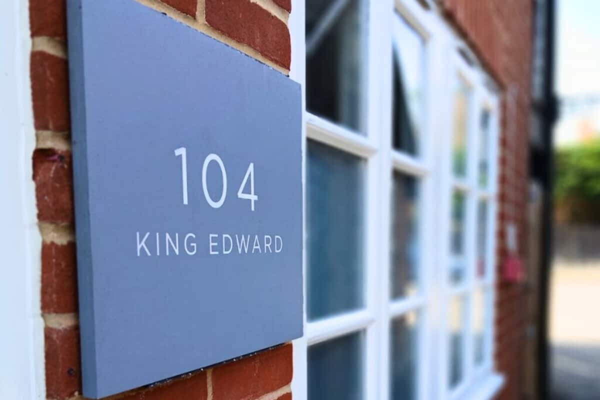 A blue house number sign with "104 KING EDWARD" on a brick wall.