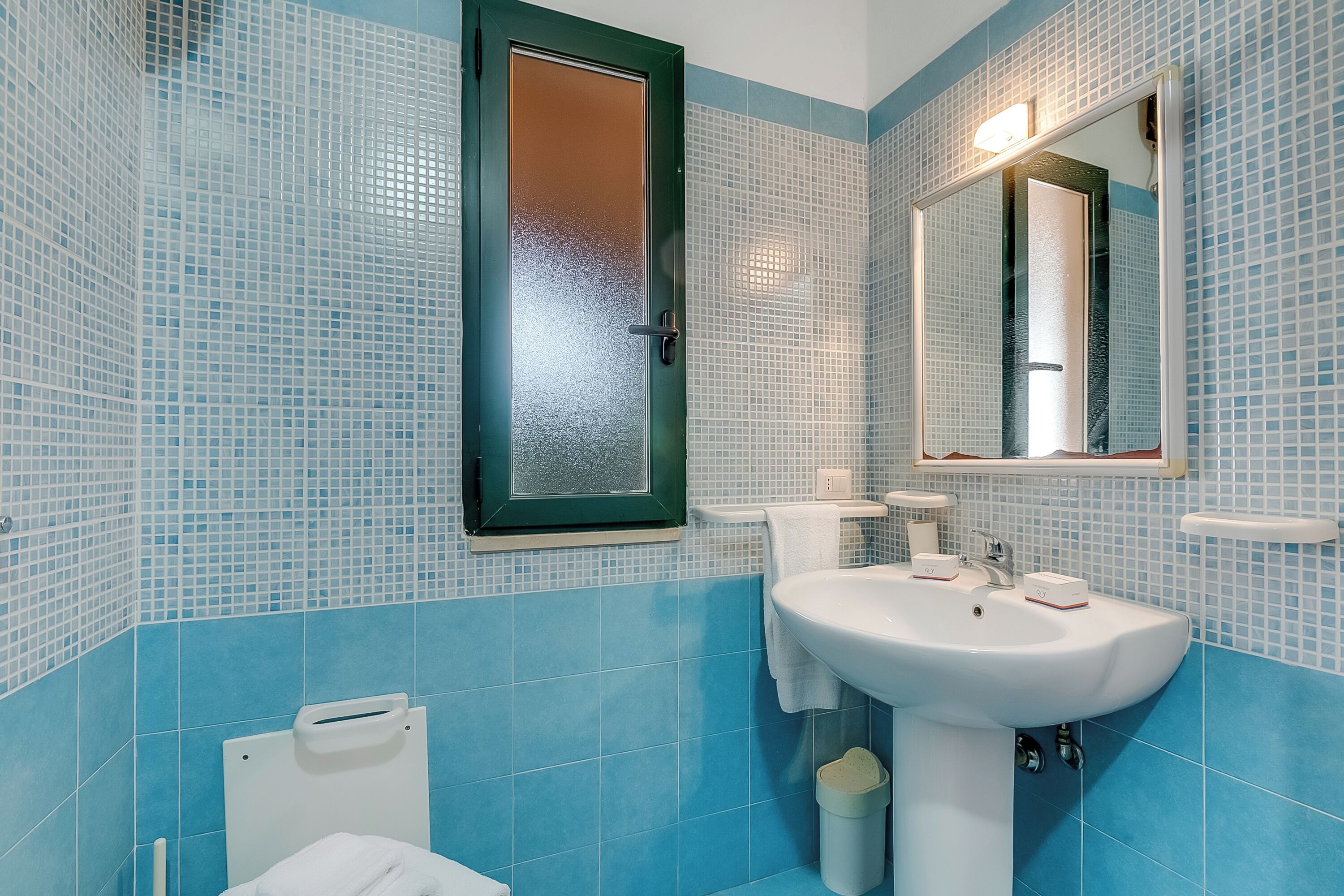 A bathroom with blue tiled walls, a white sink, and a mirror above it.