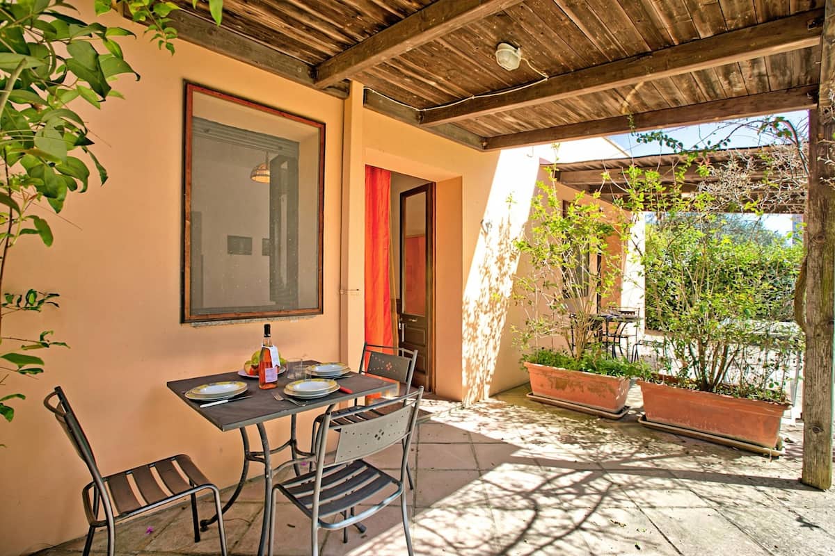 Une terrasse couverte avec une table dressée pour les repas, des chaises et des plantes en pot.