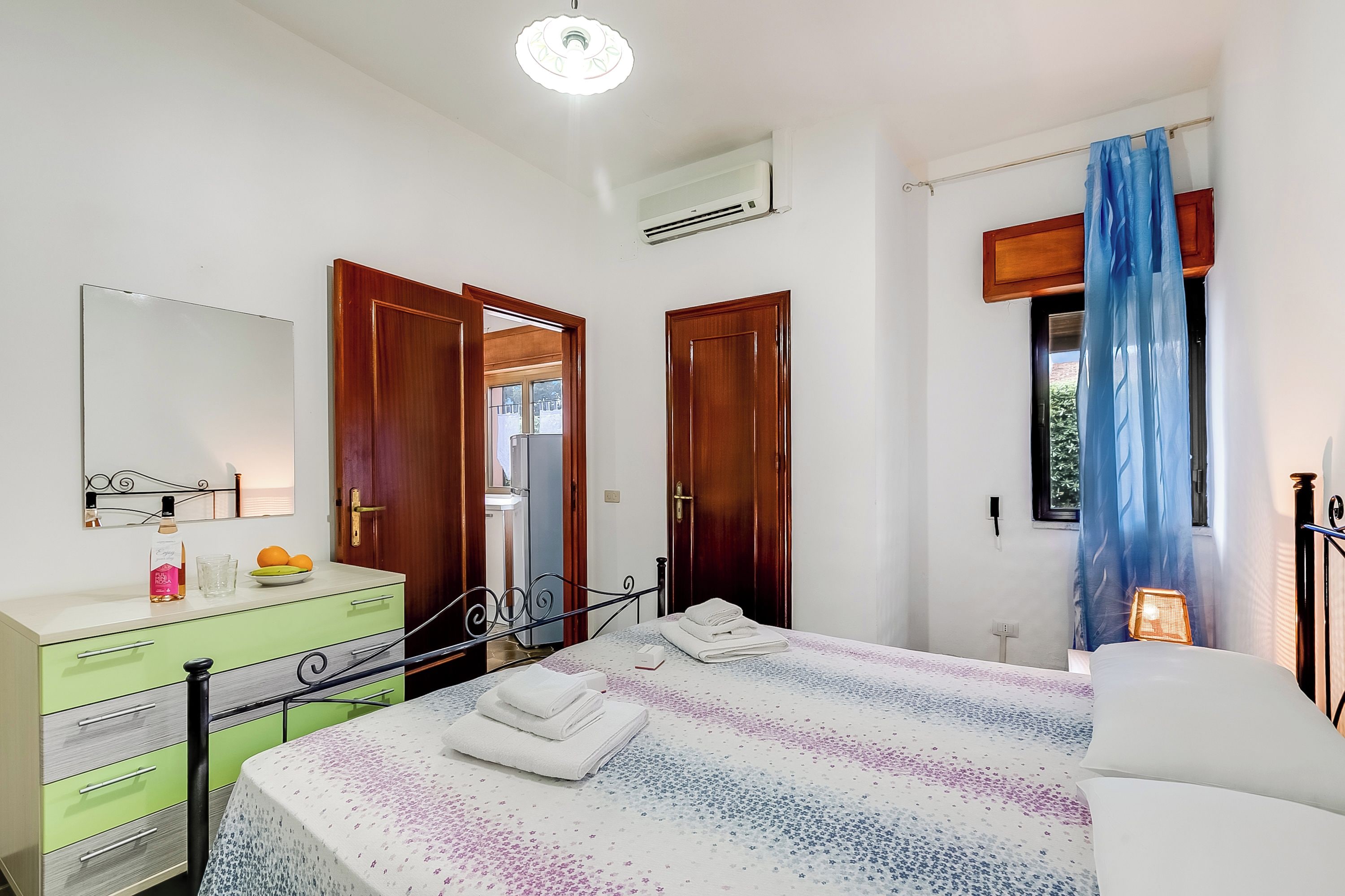 Une chambre à coucher avec un lit, une commode, un miroir et une fenêtre avec des rideaux.