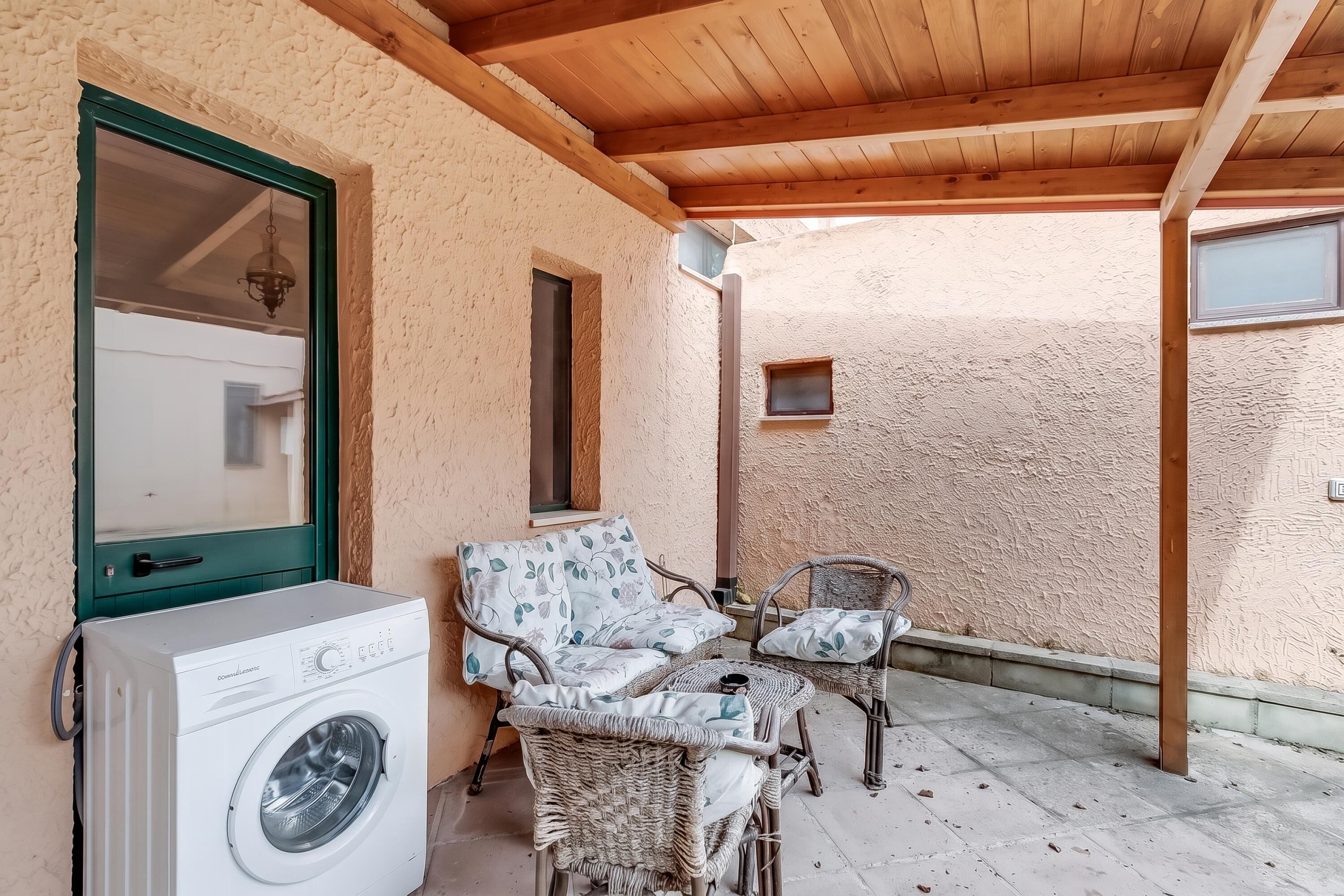 A covered outdoor area with a washing machine, wicker furniture, and a window.