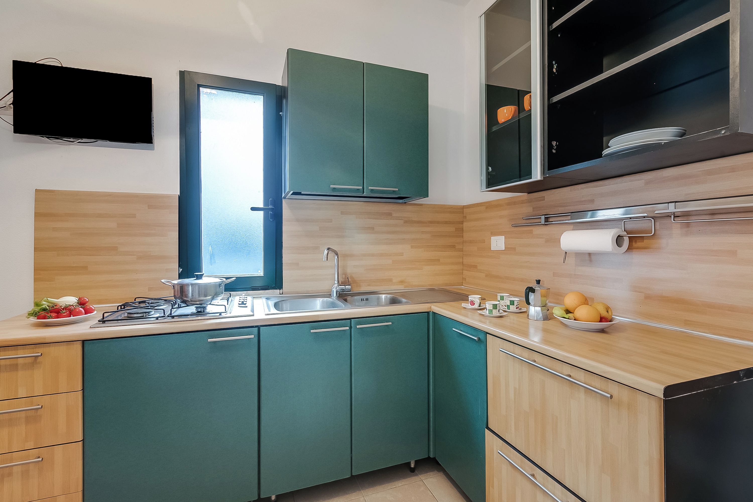 Cozinha moderna com armários verde-água, pia de aço inoxidável e janela.