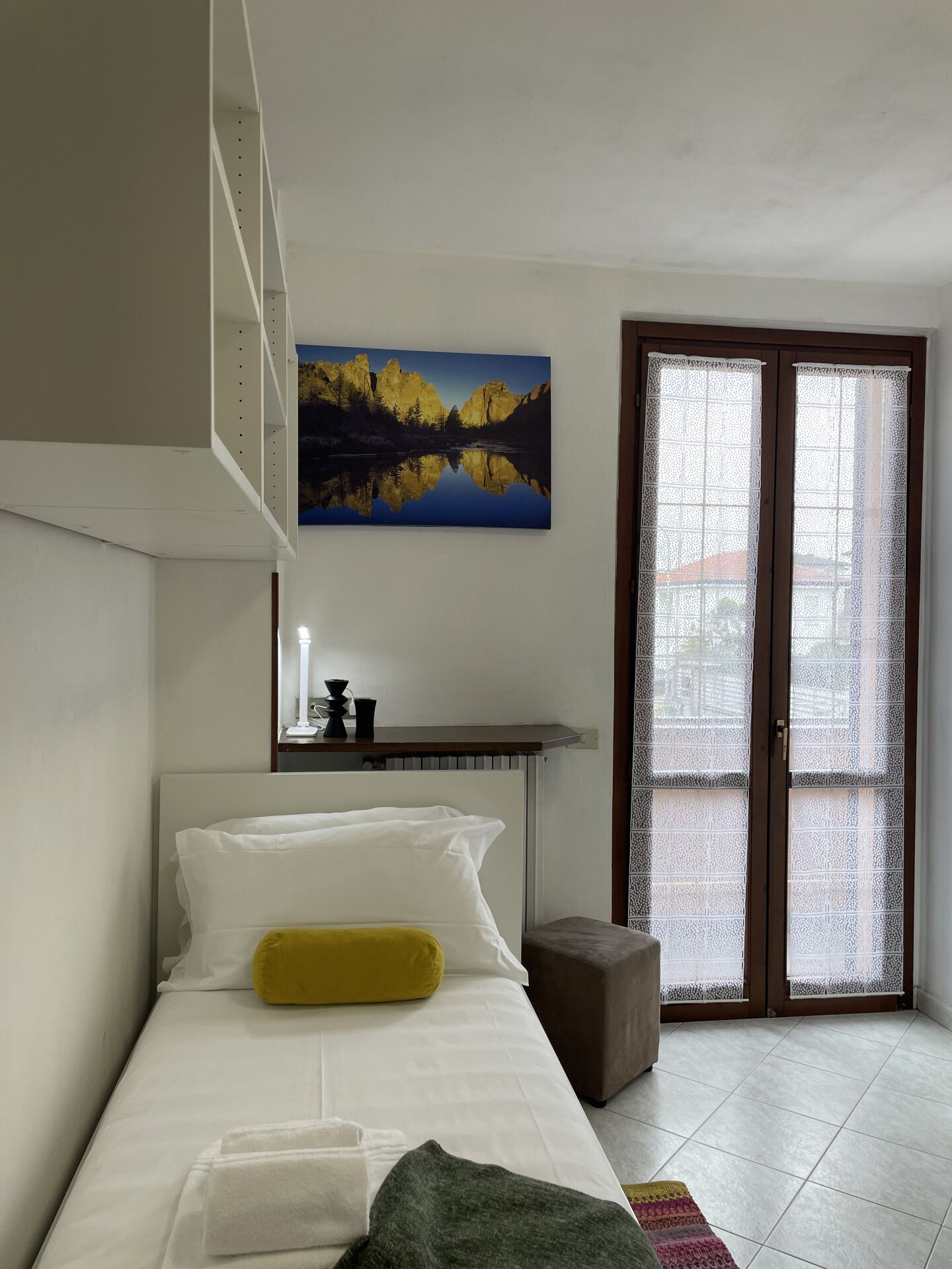 Een slaapkamer met een bed, een schilderij, een raam met geëtste glas en een radiator.