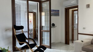 Sala de estar com uma cadeira de balanço preta, um sofá bege e uma porta de vidro deslizante que dá para uma varanda.