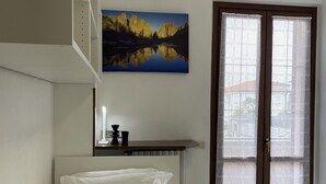 Um quarto com uma cama, uma mesa de cabeceira, um quadro de uma paisagem montanhosa e uma janela com vidro jateado.