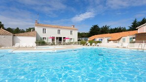 A swimming pool with clear blue water, surrounded by white buildings with tiled roofs, and a clear sky. - Maison cosy avec Terrasse, proche de la Plage! (Saint-Hilaire-de-Riez)