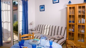 A room with a striped sofa, a dining table with blue glassware, a cabinet with glass doors, and two framed pictures on the wall. - Maison cosy avec Terrasse, proche de la Plage! (Saint-Hilaire-de-Riez)