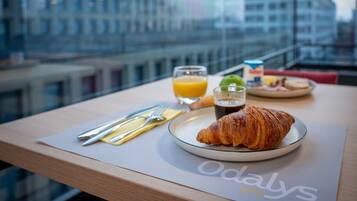 A breakfast setup with a croissant, juice, and a plate of food on a table with a view of a cityscape.