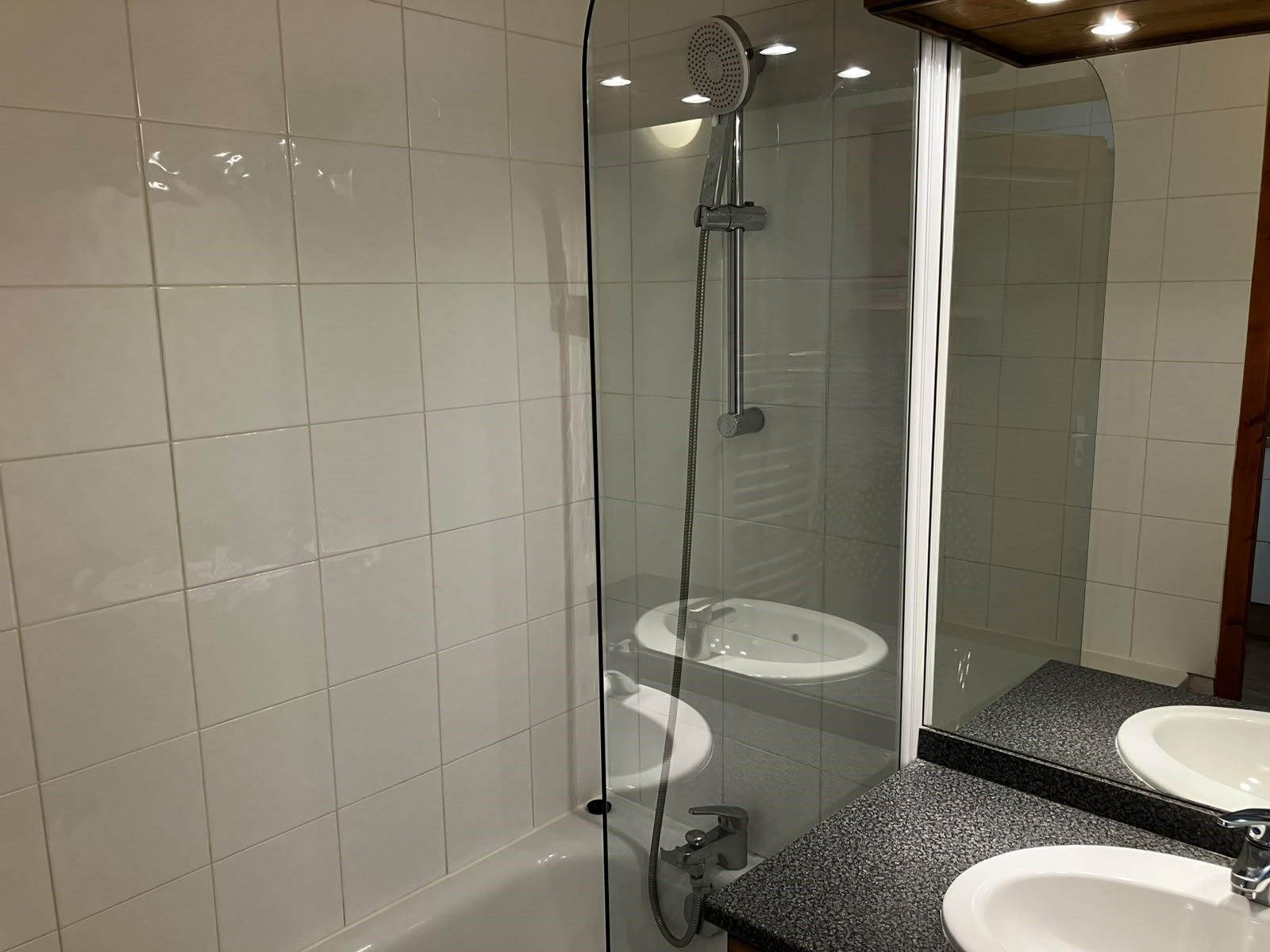 Ein modernes Badezimmer mit einer gläsernen Dusche, zwei Waschbecken und einem großen Spiegel.