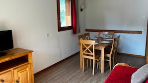 A room with a wooden desk, a dining table with chairs, a television on a stand, and a window with curtains. - Appart à 50m des Remontées | Piscine Intérieure (Val-Cenis)