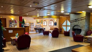 A hotel lobby with a reception desk, seating area, fireplace, and a view of the outdoor area. - Appart à 50m des Remontées | Piscine Intérieure (Val-Cenis)