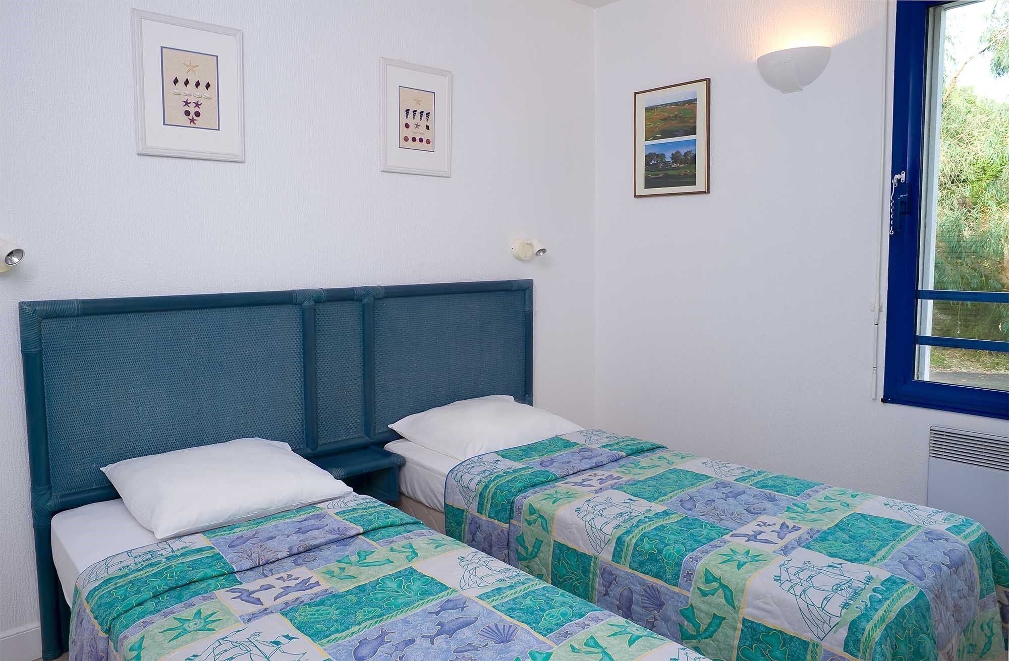 A room with two single beds, a window with a view of greenery, and wall-mounted artwork.