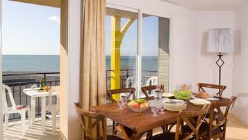 A dining area with a view of the sea, a table set with plates, glasses, and a bowl of fruit.