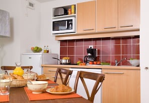 A kitchen with wooden cabinets, a microwave, a coffee maker, and a dining table set with breakfast items. - Tout près de la plage à pied! (Cayeux sur Mer)