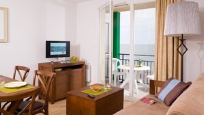 A hotel room with a dining area, a TV, a balcony with a view of the sea, and a lamp.
