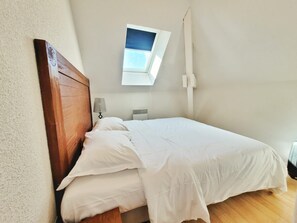Ein Schlafzimmer mit einem hölzernen Kopfteil, einem Bett mit weißer Bettwäsche, einem Nachttisch mit Lampe und einem Fenster mit Blick auf den Himmel.