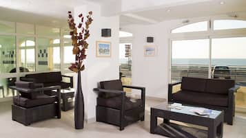 Lounge with wicker sofas, armchair, and coffee table beside large windows facing the sea