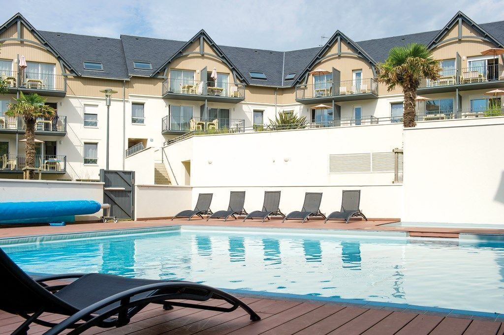 Een hotel met een zwembad, ligbedden en een palmboom.