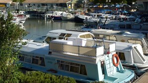 A marina with various boats docked, a bridge in the background, and a building with a tiled roof. - Maison Cosy + Piscine Extérieure Chauffée (Colombiers)
