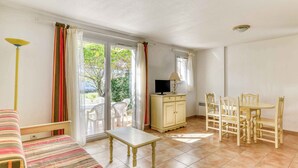 A room with a bed, a small table, a TV, and a dining area with chairs.