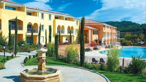 Ein Hotel mit Schwimmbad, Außengastronomie und einer Fontäne.
