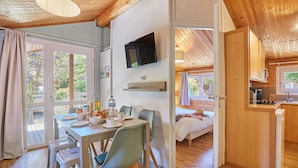 A cozy room with a dining table set for two, a bed, a TV mounted on the wall, and a kitchen area.