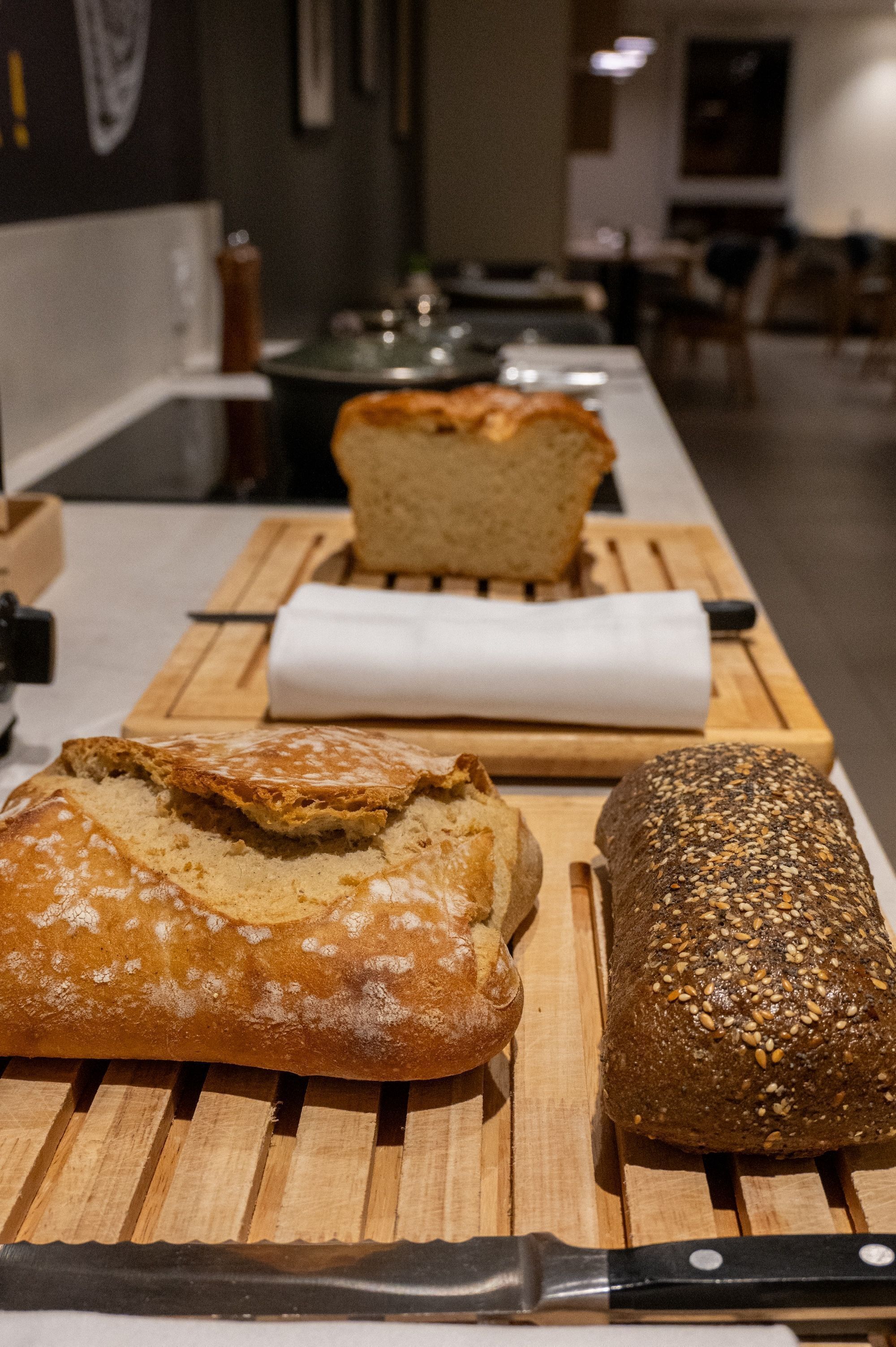 A wooden cutting board with three loaves of bread, a knife, and a white napkin.