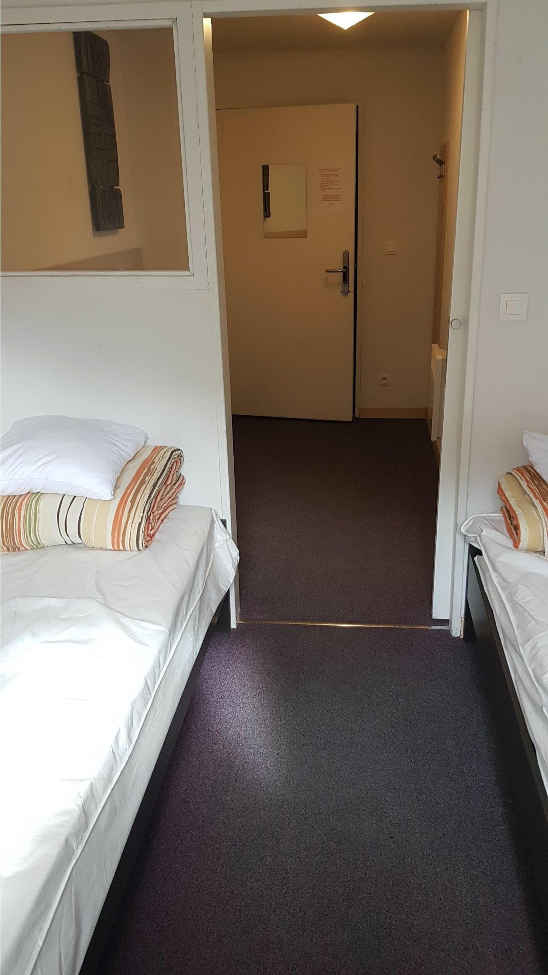 Une chambre d’hôtel avec deux lits, une porte avec une pancarte et un sol recouvert de moquette.