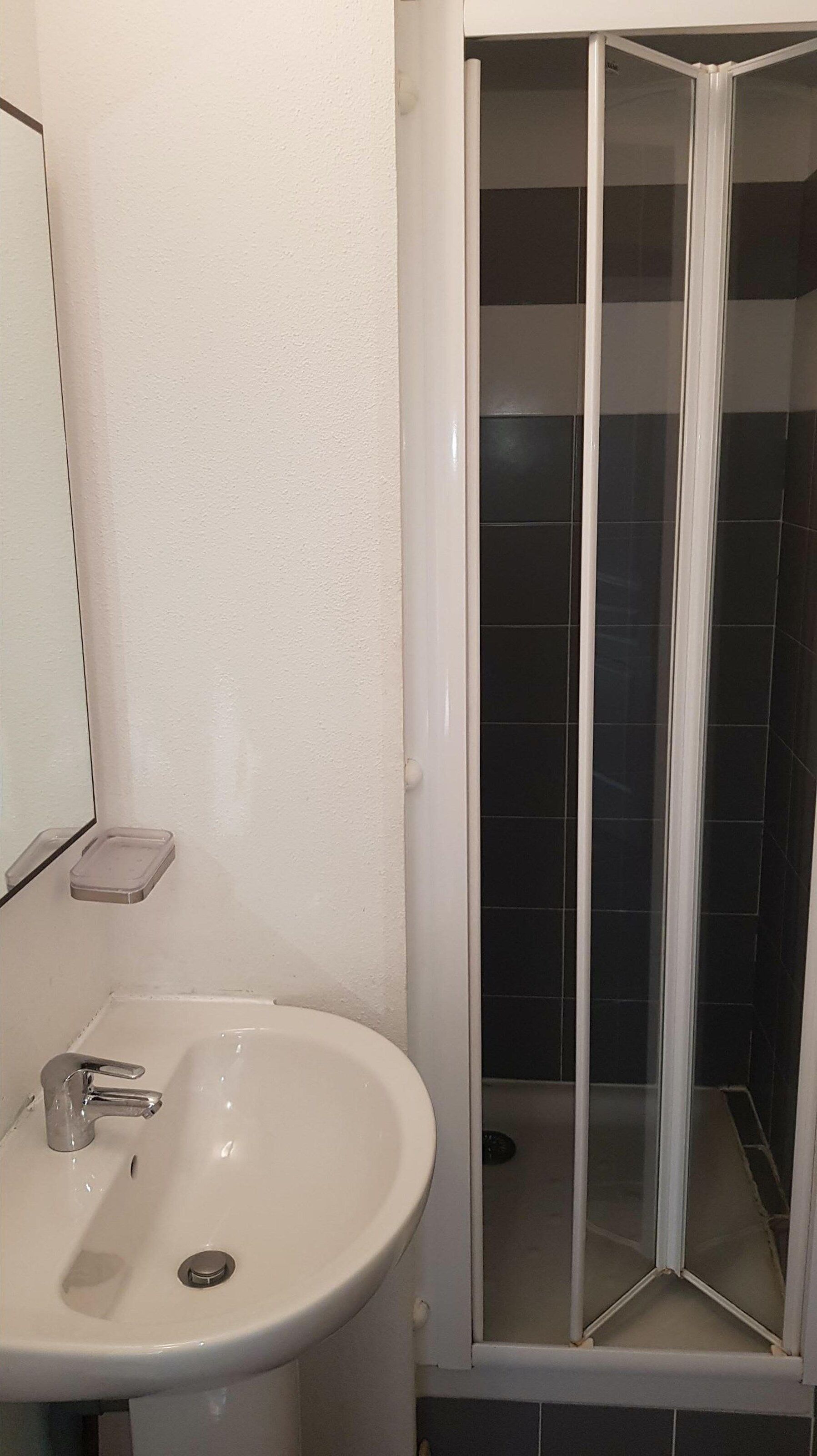 Ein Badezimmer mit weißem Waschbecken, einem Spiegel und einer Duschkabine.