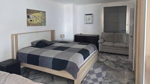 Une chambre à coucher avec un lit, des tables de chevet, un canapé et des œuvres d’art accrochées aux murs.