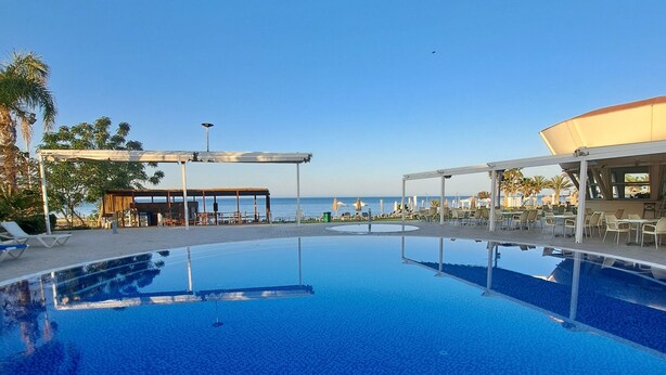 A clear blue pool with a tiled floor, surrounded by lounge chairs and umbrellas, with a view of the sea in the background. - Serenity Pearl villa with a private pool,  2 min walk to the beach (Protaras)
