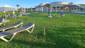 A sunny outdoor area with rows of sun loungers and umbrellas, a large building in the background, and a clear blue sky. - Serenity Pearl villa with a private pool,  2 min walk to the beach (Protaras)